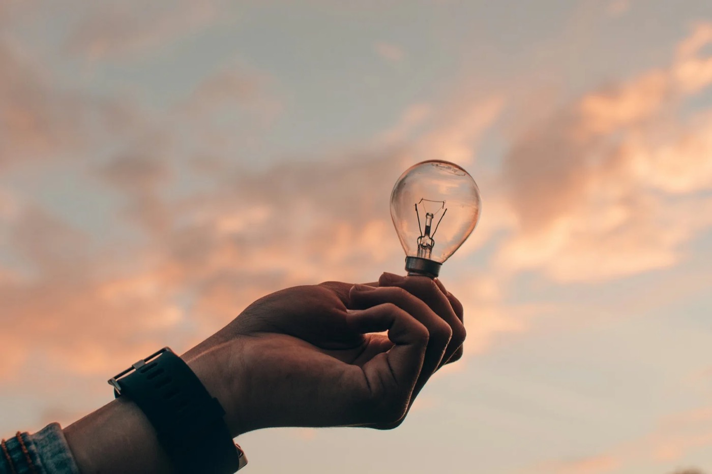 A hand holding a lightbulb against a sunset sky